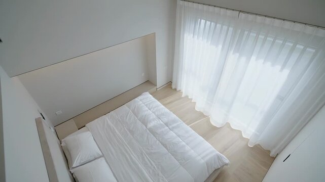 Showing overhead view of double bed with three pillows in bedroom, curtains drifting from daylight