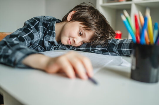 Fatigued schoolboy leaning on desk while studying at home