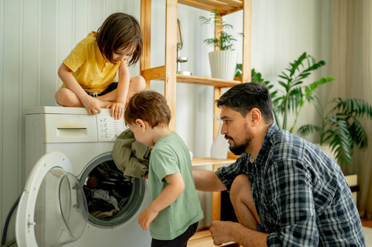 Father with children helping washing clothes in machine at home