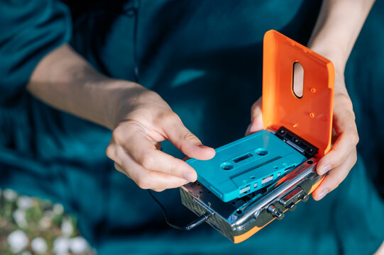 Hand inserting blue cassette into orange retro audio player outdoors