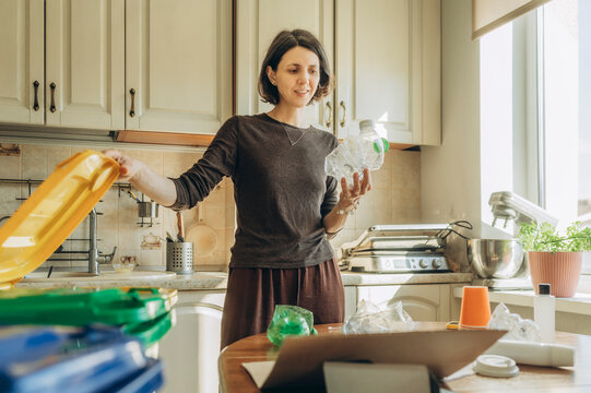 Woman sorting plastic waste into recycling bin at home