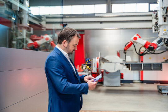 Manager using tablet in automated factory with industrial robot