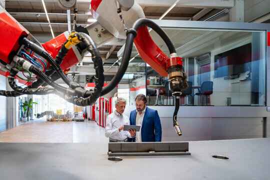 Colleagues discussing production on tablet near industrial robot