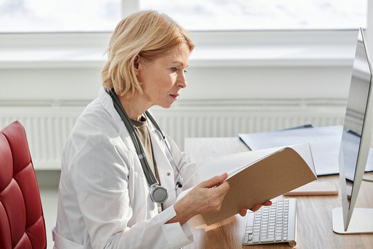 Doctor reading medical report sitting at desk in clinic