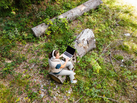 Digital nomad working on laptop sitting on a log in the forest