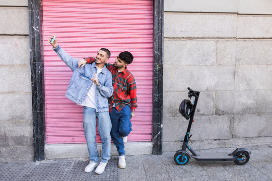 Young gay couple taking selfie using smart phone in front of roller shutter wall