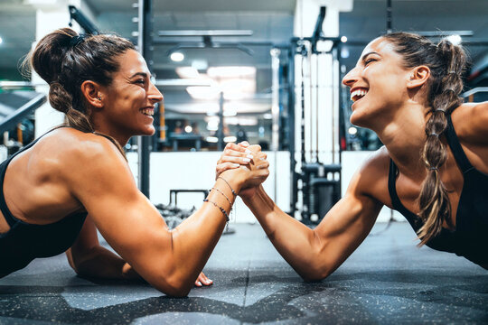 Happy female twins in good shape doing arm wrestling challenge in a gym