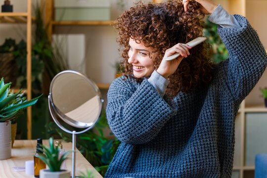 Smiling woman styling curly hair with a comb for a morning routine