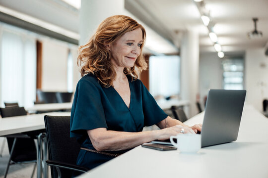 Smiling businesswoman working on laptop at conference table in board room