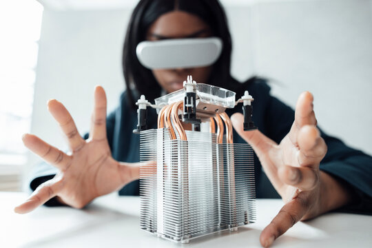 Engineer wearing virtual reality simulator gesturing at semiconductor on desk in office