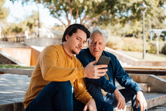 Man showing smart phone to father sitting on steps