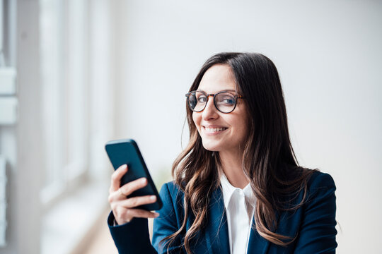 Smiling businesswoman holding smart phone at home office