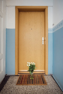 Vase with bunch of white farewell flowers on floor mat at apartment door of deceased neighbour