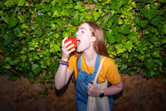 Redhead eating a red apple outdoors with flash lighting