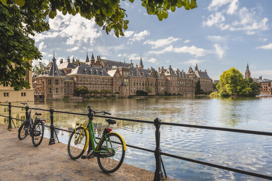 Netherlands, South Holland, The Hague, Bicycles leaning on railing of bridge stretching over Hofvijver lake canal with Binnenhof government office in background