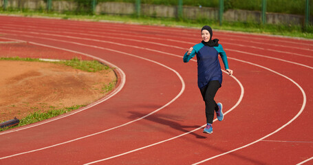 Fototapeta premium Young Muslim Woman Running on Outdoor Track in Hijab Training for Fitness and Athletics