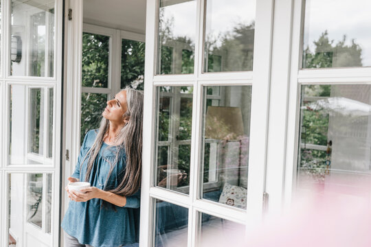 Pensive woman leaning against door case of her winter garden