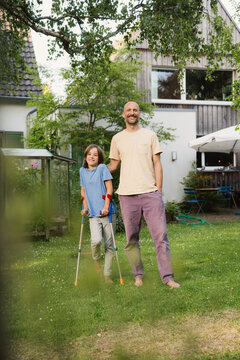 Father and son in garden during summer with crutch and injury recovery