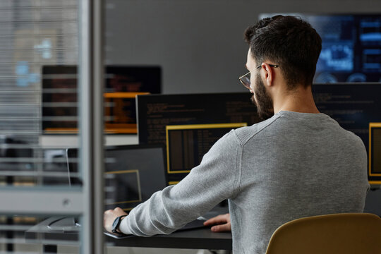 Computer programmer using laptop in front of desktop PCs
