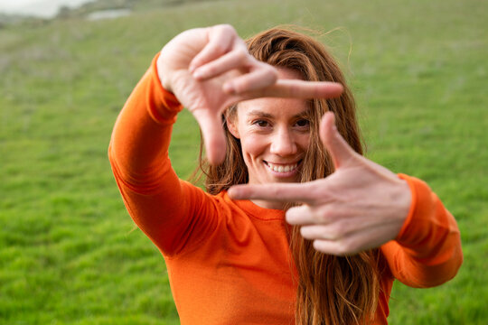 Smiling and framing face with hand in grass field in Granada