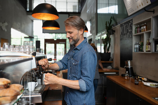 Smiling barista steaming milk in cafe