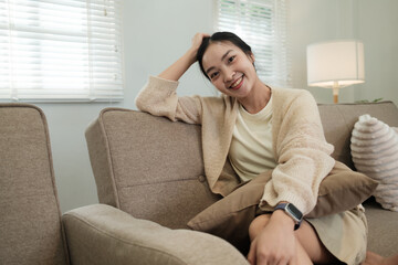 Fototapeta premium Young Asian woman smiling broadly relaxing on sofa at home