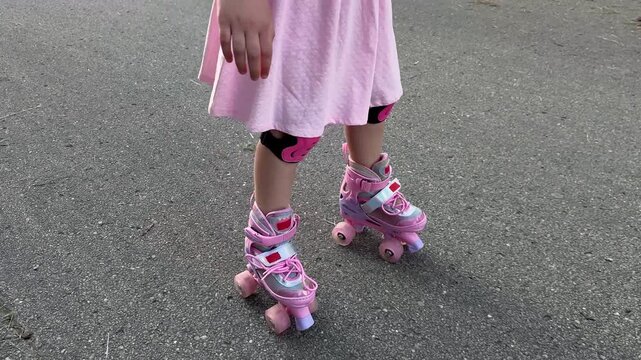 Cropped view of child feet in retro style quad rollerskates with pink wheels and safety pads on a park road