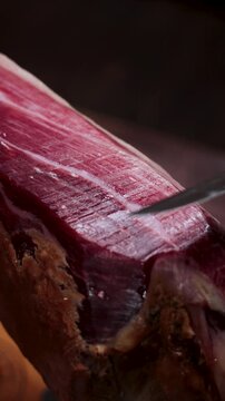 Hand slicing thin delicate pieces of delicious serrano ham from a whole cured pork leg