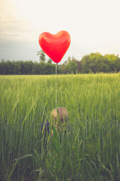 Little boy with red heart-shaped balloon hiding in a field