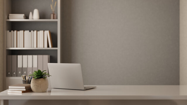 Laptop with book and pencil beside potted plant on white table in front of shelf in grey wall office