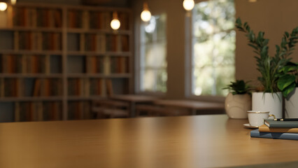 Wooden table with coffee cup and book beside potted plant across bookshelf and window in dim library © bongkarn