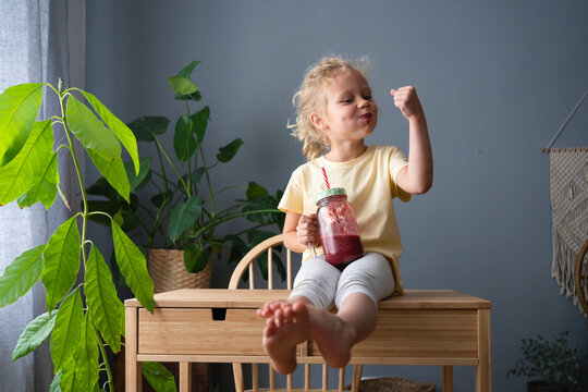 Girl drinking healthy fruit smoothie flexing muscles at home