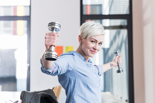 Portrait of smiling woman exercising with dumbbells in office