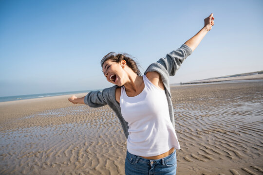 Carefree young woman with arms outstretched at beach against clear sky