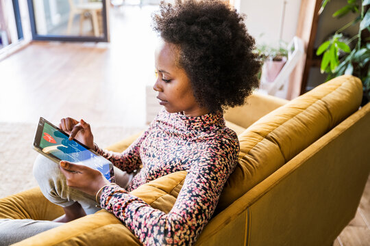 Woman sitting on sofa at home checking blood pressure on tablet
