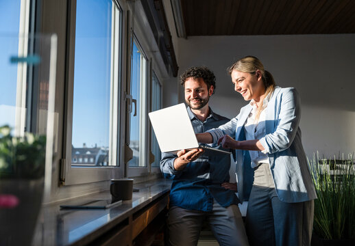 Smiling businessman and businesswoman brainstorming with laptop