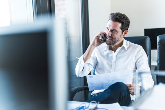 Businessman talking on mobile phone holding document in office