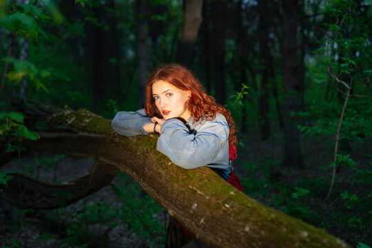 Red-haired model in denim jacket leaning on a mossy tree