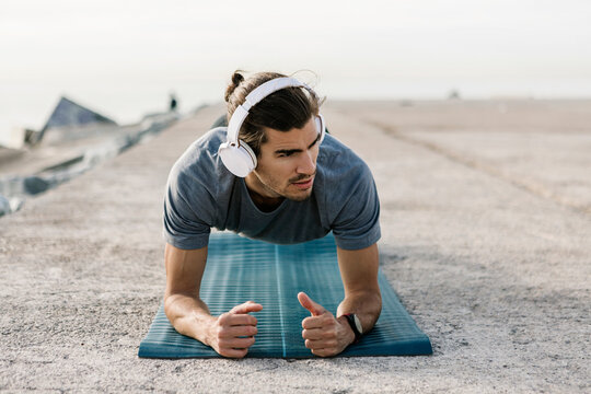 Young sportsman with headphones practicing plank position on exercise mat