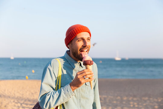 Smiling tourist licking ice cream cone on sunny Barcelona beach