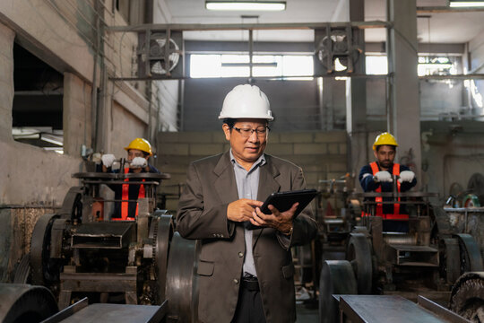 Senior Asian industrial engineer using digital tablet to inspect factory production line background.