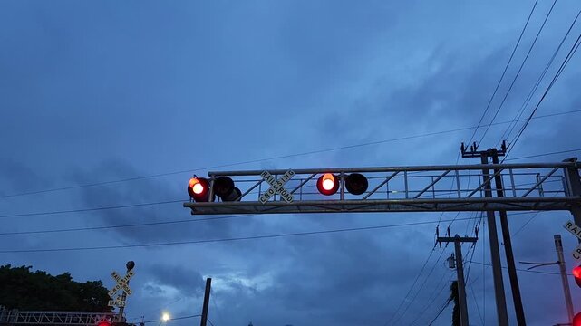 Video footage featuring a close-up view of illuminated railroad crossing warning lights and crossbuck sign during train passage. The tops of train cars are visible beneath the signal structure while d