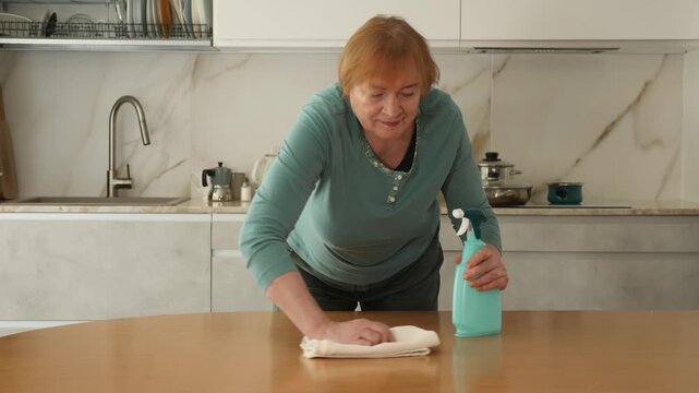 Mature woman poses with washcloth and disinfect spray.Senior lady plans wiping messy dirty cooking counter for housekeeping housework or chores.