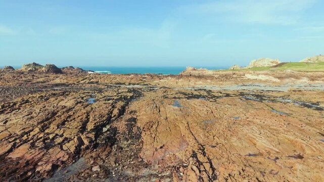 La Grosse Rocque beach Cobo Bay Guernsey.Panning low drone footage of amazing pink granite foreshore with rockpools at low tide in late afternoon sun with clear blue sky
