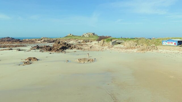 La Grosse Rocque beach Cobo Bay Guernsey.Panning across glorious sandy beach with golden sand and granite rocks,calm sea,old military fort in the background in late afternoon sun with clear blue sky