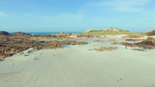 La Grosse Rocque beach Cobo Bay Guernsey.Panning across glorious sandy beach to rocky foreshore with rockpools ,backdrop of old military fort at low tide in late afternoon sun with clear blue sky