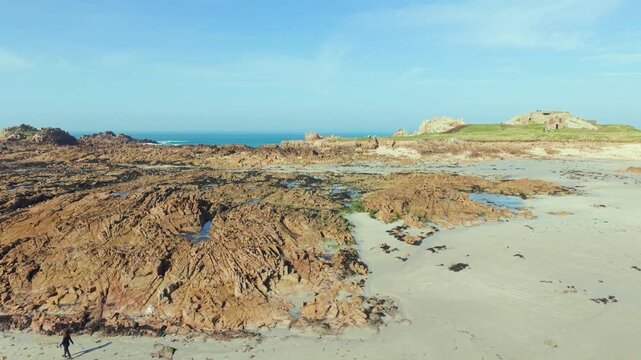 La Grosse Rocque beach Cobo Bay Guernsey.Panning across sandy beach and amazing pink granite foreshore with rockpools ,backdrop of old military fort at low tide in late afternoon sun