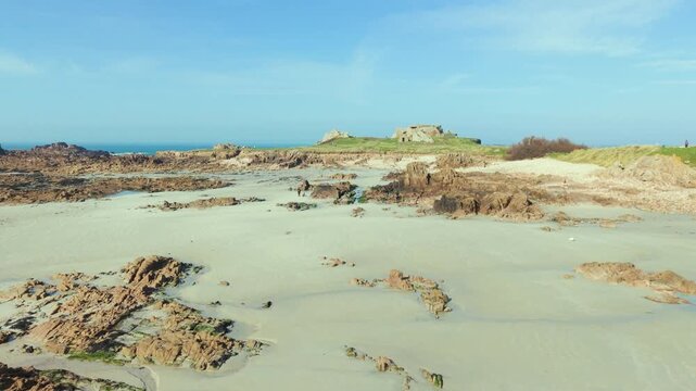 La Grosse Rocque beach Cobo Bay Guernsey.Panning across glorious sandy beach with golden sand and granite rocks,circling old military fort at low tide in late afternoon sun with clear blue sky