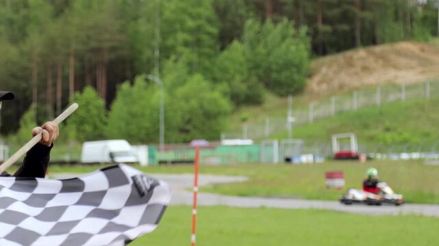 Close-up of a checkered flag at a go-kart circuit. Symbol of race completion, victory and competition in motorsport, with blurred karts and track in the background.