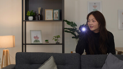 Young Asian Woman Exploring Dim Living Room with a Bright Flashlight © blueringmedia